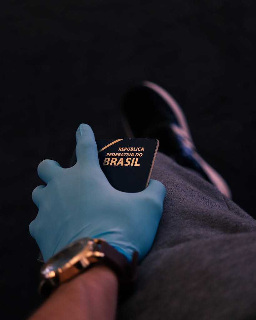 A person wearing a blue glove holding a Brazilian passport, emphasizing health safety during travel.